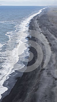 Black volcanic sand beach with white foam and blue sea. Vik, Ice