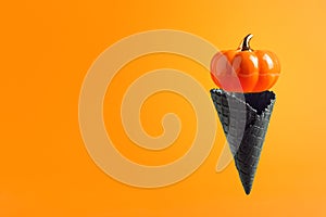 Black waffle ice-cream cone with big pumpkin levitating on orange background. Halloween holiday concept