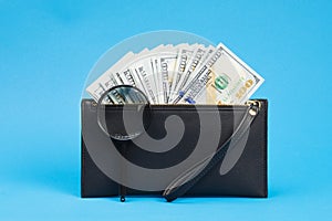 Black wallet with one hundred dollar bills and two hundred euro bil on a blue background. Checks dollar bills with a magnifying