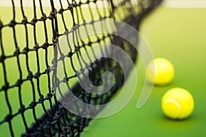 Black weaved net and two tennis balls on green hard court