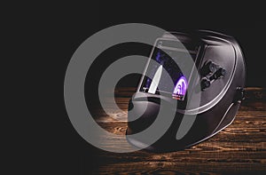 Black welding mask on a wooden background. A studio photo with hard lighting