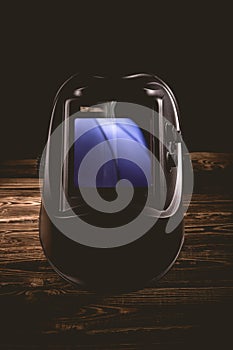 Black welding mask on a wooden background. A studio photo with hard lighting