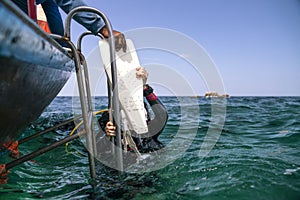 A black wet suit sucuba diving woman give fin to boatman before get on the boat