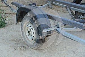 A black wheel and part of a gray iron frame of a car trailer