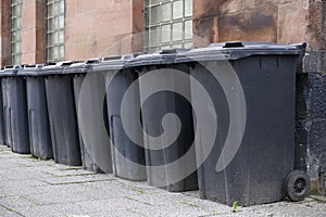 Black wheelie bins in a row on street with house numbers printed on front waiting for bin men to collect