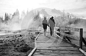 Black and white abstract landscape with people standing crossing on wooden bridge in sunrise lake with fog and hot springs at