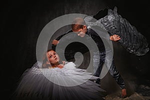 Black and white angel together on a dark background with colored lighting. The concept of war between good and evil. Girl and boy