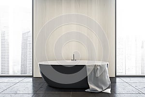 Black and white bathroom with white bathtub and towel near window