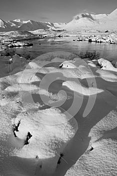 Black and white Beautiful Winter landscape image looking towards Scottish Highlands mountain range across Loch Ba on Rannoch Moor