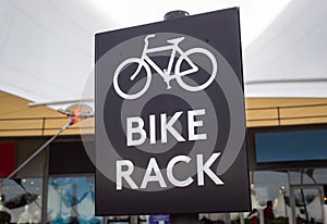 Black and white bike rack sign close up in busy urban shopping area.