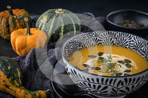 Black-and-white bowl with pumpkin soup, cream and seeds on black background