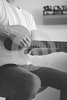 Black and white candid portrait of an artist strumming a guitar at home. He enjoys every chord played. Close-up on a hand playing