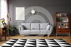 Black and white carpet with geometric pattern placed on the floor in dark living room interior with grey couch, vintage cupboard