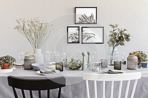 Black and white chair at table with tableware in grey dining room interior with posters