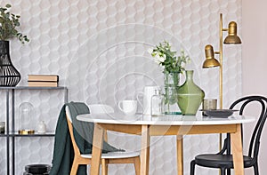 Black and white chair at wooden table in dining room interior with flowers and gold lamp. Real photo