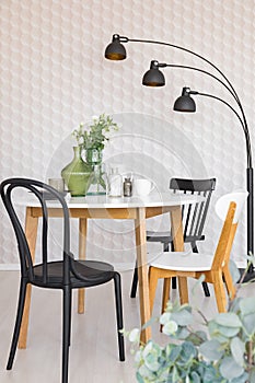 Black and white chair at wooden table in dining room interior with plants and lamp. Real photo