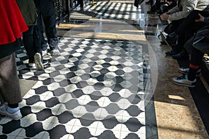 Black and white checkered floor grunge tiles marble surface at public place with interiors and people legs