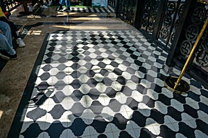 Black and white checkered floor grunge tiles marble surface at public place with interiors and people legs