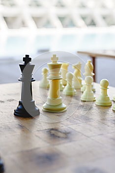 Black and white chess kings faced between defocused pieces on wooden board