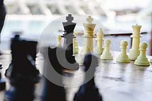 Black and white chess kings faced between defocused pieces on wooden board