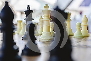 Black and white chess kings faced between defocused pieces on wooden board