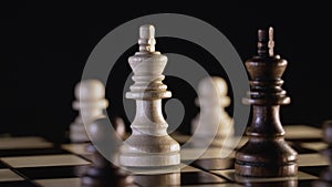 Black and white chess kings rotating on wooden board. Close-up view of pieces on chessboard on dark background. Sport