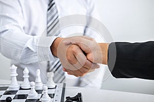 Black and White chess with player, Businessman and Businesswoman shaking hands after end game of thinking strategy to moving chess