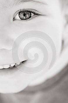 Black and white close-up half face portrait of a cute boy of three years old looking with interest and smiling, vertical image