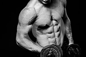 Black and white close-up of handsome power athletic mans hand stomach abs in training pumping up muscles with dumbbells