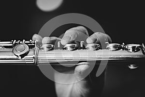 A black and white close up portrait of the fingers of a hand of a flutist musician pressing down on the valves of a metal silver