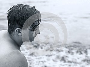 Black-and-white close up profile of young handsome man on the sea background. Wet curly dark hair. Loneliness and blue condition,