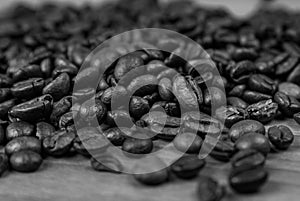 Black and white close up view of piled up roasted coffee beans on a wooden surface
