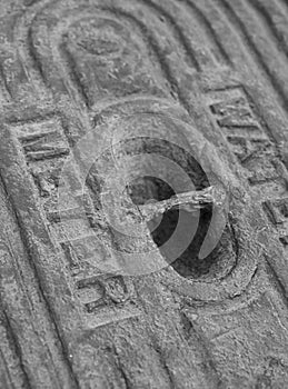 A black and white closeup detail of an old steel water meter cover dug out of the ground
