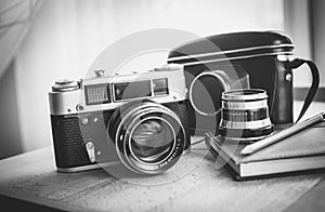 Black and white closeup photo of old camera and notebook on desk