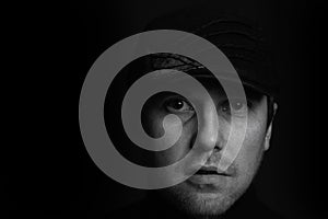 Black and white closeup portrait of an unshaven serious young gangster man with a cap on a dark background