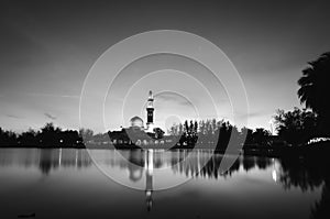 Black and white concept of beautiful floating mosque on the lake surrounded by tree and coconut tree during sunset.