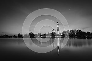 Black and white concept of beautiful mosque surrounded lake and coconut tree during sunset.