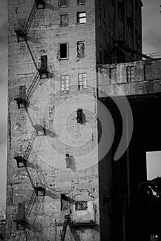 Black and white conceptual photo of an old factory building. A concrete structure with metal stairs and broken windows.