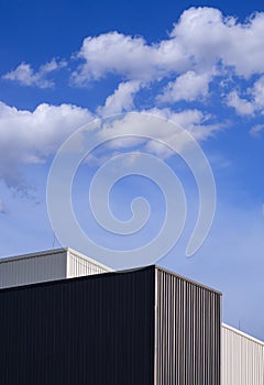 Black and white corrugated metal factory buildings against clouds and blue sky background in vertical frame