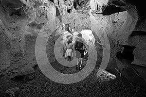 Black and white. Couple of tourists exploring the cave. The interior of the cave. Touristic hiking route. Concept of excursions photo