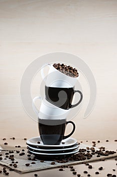 Black and white cups on the stack of the plates with full of roasted coffee beans standing on newspaper.