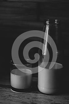 Black and white photo of half a bottle of fresh milk and poured in a glass a wooden background