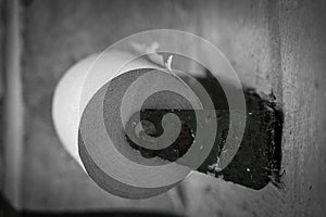 Black and white desaturated photograph of a roll of thin single ply toilet paper on a rusty toilet paper holder