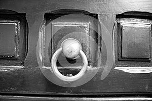 Black and white detail of old wooden external door with brass knocker
