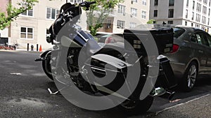 Black and white easyrider motorcycle sits on its kick stand as a classic car drives past