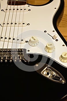 Black and white electric guitar details. Closeup: Body, bridge, single coil pickups, strings, jack, knobs, switch and pickguard.