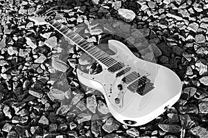 Black and white electric guitar on the railroad tracks and stone