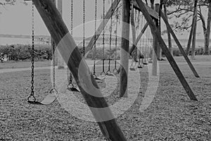 Black and white empty abandoned swings in a local park reflect our forgotten childhood