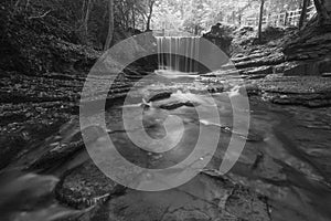 Black and white Epic beautiful Autumn landscape image of Nant Mill waterfall in Wales with glowing sunlight through the woodland