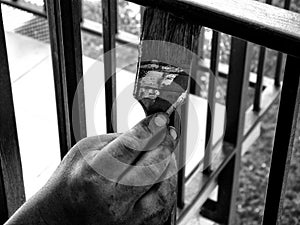 Black and white finished painter`s hand with brush painting steel corridor railing. selective focus.